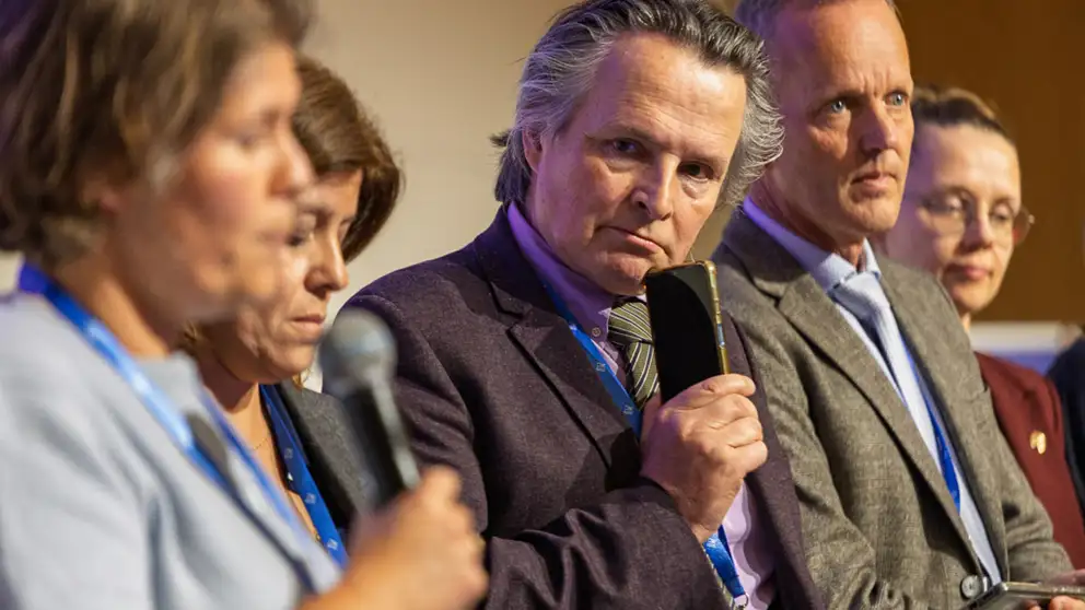 Women speaking in microphone. People in the background are listering to her.