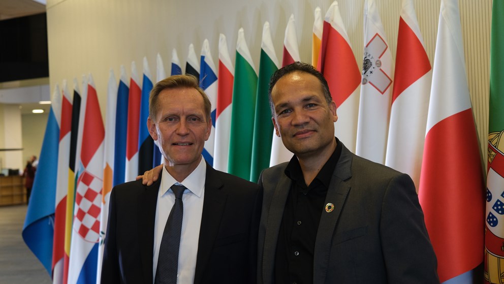 Two men in front of flags